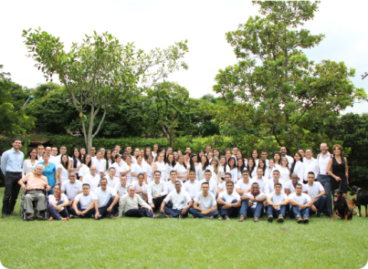 Grupo de colaboradores de Allers Group reunidos en un espacio verde, vestidos con camisa blanca y fondo natural de árboles.