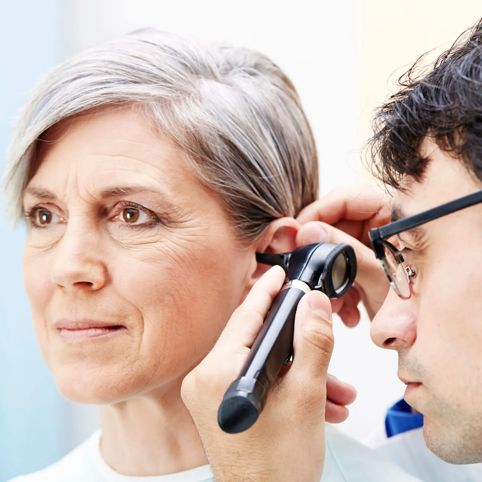 Médico examinando el oído de una mujer mayor utilizando un otoscopio Welch Allyn, en consulta médica.