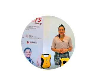 Presentadora explicando el funcionamiento de un desfibrilador externo automático en un espacio corporativo.