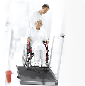 Paciente en silla de ruedas siendo pesado en plataforma médica digital Seca.